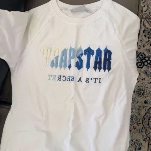 Vit Trapstar t-shirt med broderi - Vit t-shirt från Trapstar med broderad logga i blå och vita nyanser på bröstet. Klassisk passform och korta ärmar, perfekt för en streetwear-look. Materialet känns mjukt och skönt mot huden.