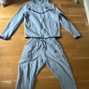 En grå nike tech byxorna storlek 147-158 hoodie storlek 158-170  - Snygga grå mjukisbyxor från Nike med svart logga på benet. Byxorna har elastisk midja med snörning och är tillverkade i mjukt bomullsmaterial. Perfekta för chill eller träning, med en loose fit och klassisk sportig look.