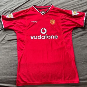 Manchester United Beckham 7 tröja - Klassisk Manchester United-matchtröja från Umbro med Beckham 7 på ryggen. Röd med vita och svarta detaljer, Premier League-märken på ärmarna och Vodafone som sponsor. Broderat klubbmärke på bröstet. Tillverkad i lätt och ventilerande polyester. Helt nytt, har inte använt innan.