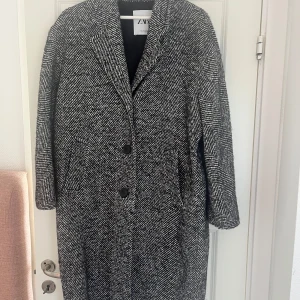 Svartvit kappa från Zara - Säljer en svartvit kappa från Zara i storlek S. Den har ett snyggt mönster, klassisk krage och tre stora knappar framtill. Perfekt för höst och vinter, med lång ärm och en rak, lite oversized passform. Materialet känns mjukt och varmt.