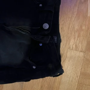 Svarta bootcut jeans från ONLY - Snygga svarta jeans från ONLY med bootcut-modell och klassisk femficksdesign. Jeansen har dragkedja och knapp framtill samt subtila slitningar längs benen för en cool look. Perfekta för dig som gillar en tidlös och trendig stil.