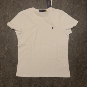 Helt ny Vit t-shirt från Polo Ralph Lauren storlek S - Det står att den är L men det är felmärkning den är storlek S. Vit t-shirt från Polo Ralph Lauren med klassisk rund hals och korta ärmar. T-shirten har en liten mörkblå broderad logga på bröstet och är gjord i mjuk bomull. Enkel och stilren modell som passar till allt.