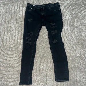 Svarta skinny jeans Jack & Jones - Svarta Jeans från Jack & Jones, modell Liam. Jeansen har slitna detaljer och trasiga partier på benen.