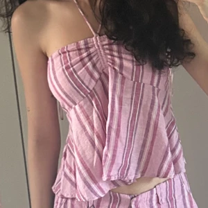 Randig rosa linnetopp från Bershka - Superfin randig linnetopp från Bershka i olika nyanser av rosa och vitt. Toppen är ärmlös med bandeau-modell, smockad rygg och tunna axelband som knyts i nacken. Luftig och flowy passform, perfekt för varma dagar. Har sytt där bak. Använd vid 2 tillfällen. 