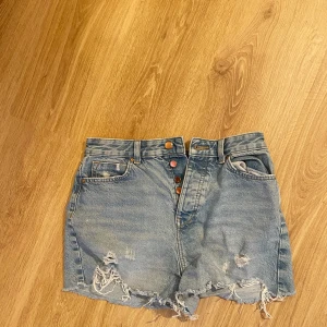  jeansshorts från Zara - Snygga ljusblå jeansshorts från Zara med råa, fransiga kanter. Shortsen har slitna detaljer framtill, klassiska fem fickor och knappar i gylfen. Perfekta för varma sommardagar och en avslappnad look.