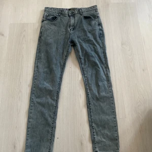 Grå skinny jeans från Armani - Snygga grå jeans från Armani med klassisk femficksdesign och silverfärgade detaljer. Byxorna har smal passform och ikoniska Armani-loggor på bakfickan och knappen. Perfekta för dig som gillar stilrena och exklusiva jeans med en modern vibe.
