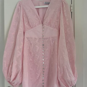 Ljusrosa blommig klänning från Adoore - Florence dress från Adoore med broderade blommor, v-ringning och långa puffärmar. Klänningen är från Adoores senaste släpp av Florence modellen som är helt slutsåld på hemsidan. Klänningen är inte använd och har prislapp kvar