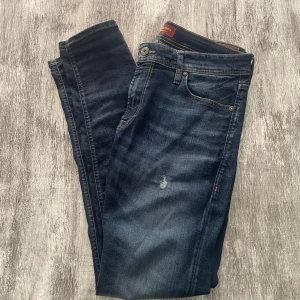 Mörkblå jeans från Jack & Jones - Snygga mörkblå jeans från Jack & Jones med klassisk femficksdesign och diskreta slitningar framtill. Jeansen har modell Skinny/Liam, tillverkade i mjukt jeanstyg som sitter skönt hela dagen. Perfekta för en avslappnad och stilren look.