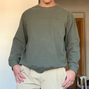 Vintage Olivgrön sweatshirt - Olivgrön sweatshirt från Arrow i storlek L. Tröjan har en klassisk rund halsringning, ribbade muddar och avslut. Tröjan är tyngre och slitstark. Tillverkad i mjuk bomulls mix, perfekt för en chill och avslappnad stil. Enkel och stilren design utan tryck eller mönster.