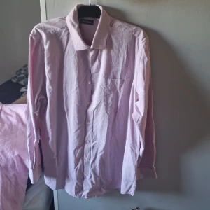 Ljuslila skjorta från Dressmann 2XL - Snygg ljuslila skjorta från Dressmann i storlek 2XL. Skjortan har klassisk krage, bröstficka och knäppning framtill. Materialet är bomull och känns mjukt mot huden. Perfekt för dig som gillar stilrena och enkla plagg med en fräsch färg.
