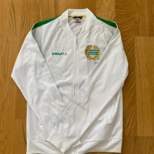Vit Hammarby Craft jacka S - Vit jacka från Craft med Hammarby IF:s broderade klubbmärke på bröstet och gröna detaljer på axlarna. Jackan har dragkedja framtill och är tillverkad i polyester, perfekt för dig som vill representera Bajen på match eller i vardagen. Nypris:599 mittpris 299 priset är ej hugget i sten. Hör av er vid minsta lilla fundering 
