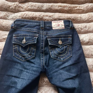 True Religion Becca Bootcut Jeans, mörkblå - Mörkblå true religion jeans, modellen är Becca mid Rise bootcut och storleken är 24. Innerbenslängd: ca 80cm och tvärs över midjan är de ca 34cm 💗De är använda ett fåtal gånger och är i bra skick 💞