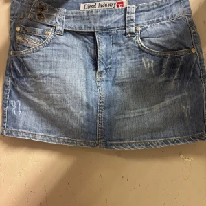 Lågmidjad jeanskjol från Diesel - Supersnygg ljusblå jeanskjol från Diesel med slitna detaljer och klassiska fickor både fram och bak. Kjolen har bälteshällor, dubbla knappar i midjan och dragkedja. Perfekt för dig som gillar en cool och avslappnad stil. 2000-tal. PS säljer samma på Vinted, @lissan17 och kan sänka priset mer där eftersom de inte tar ut en avgift som Plick gör. 