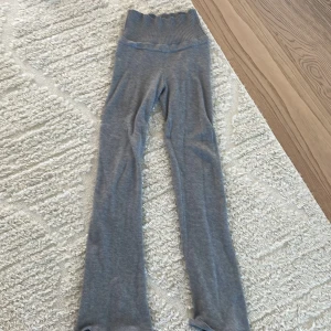 Grå stickade mjukisbyxor Gina Tricot - Mysiga grå mjukisbyxor från Gina Tricot i stickad bomullsblandning. Byxorna har hög midja med bred ribbad mudd och raka ben med lite utsvängd passform. Perfekta för chill dagar hemma eller när du vill vara extra bekväm.