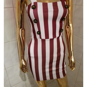 NY Randig kortklänning från Stylewise - Snygg kortklänning från Stylewise med breda vinröda och vita ränder. Klänningen är tight och har dekorativa stora knappar framtill. Axelbandslös modell som ger en cool och trendig look. Perfekt för dig som vill sticka ut med ett statementplagg.