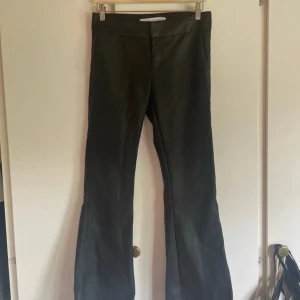 Svarta bootcut byxor i skinnimitation - Snygga svarta byxor i skinnimitation med bootcut-modell och låg midja. Byxorna har en stilren look utan synliga detaljer och passar perfekt till en trendig outfit. Materialet ger en cool känsla och de sitter riktigt bra på höfterna.