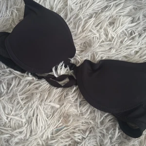 Svart bh med ett axelband - En svart bh med vadderade kupor och justerbara axelband. Enkel och stilren design utan mönster, perfekt att bära under andra plagg eller som den är. Mjuk och stretchig känsla.