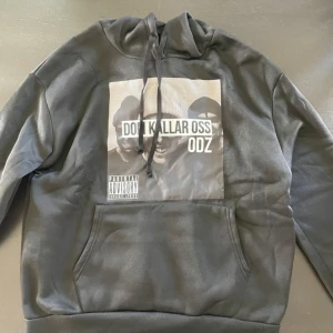 Svart hoodie med ODZ-tryck - Svart hoodie med stort grafiskt tryck på bröstet från ODZ. Tröjan har huva med snörning och en klassisk känguruficka framtill. Perfekt för dig som gillar streetwear och vill sticka ut med en fet design. Storlek xs/s