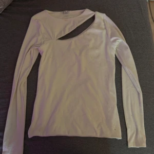 Vit långärmad topp med cut out - Trendig vit långärmad topp med unik cut out-detalj vid halsen. Snygg och stilren design som passar perfekt till jeans eller kjol. Toppens material känns mjukt och följsamt mot huden.