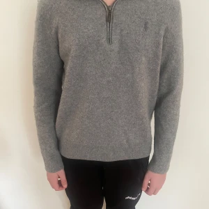 Grå halvziptröja från Ralph Lauren - Snygg grå stickad tröja från Ralph Lauren med half zip-dragkedja och diskret logga på bröstet. Tröjan har lång ärm och är i mjukt ullmaterial, perfekt för kyliga dagar. Enkel och stilren design som funkar till det mesta. Storlek L men har krympt till xxs/xs.