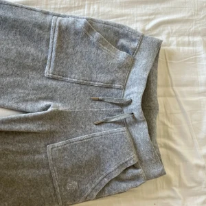 Grå mjukisbyxor Juicy Couture XS - Supermysiga grå mjukisbyxor från Juicy Couture med stora fickor fram och bak, snörning i midjan och coola silverknappar på bakfickorna. Perfekta för chill dagar eller när du vill vara bekväm men ändå snygg.