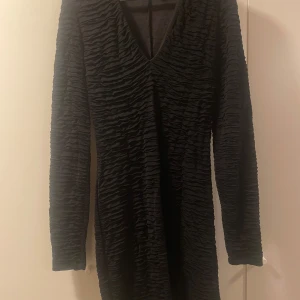 Svart långärmad klänning H&M S - Svart kortklänning från H&M i storlek S med lång ärm och snygg v-ringning. Klänningen har ett coolt rynkat tyg som ger en unik struktur och passar perfekt när du vill sticka ut lite extra.