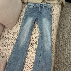 Bootcut jeans från SHEIN, ljusblå - Säljer ett par ljusblå bootcut jeans från SHEIN i storlek S (EU 36). Jeansen har klassisk femficksdesign, snygga slitningar framtill och bakfickor med dekorativa sömmar och nitar. Perfekta för dig som gillar en retro vibe och bekväm passform.