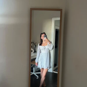 Blommig kortklänning från Hollister - Supersöt kortklänning från Hollister i ljusblått och vitt med småblommigt mönster. Klänningen har långa ärmar, volangkant nertill och söt knytning vid bysten. Perfekt för sommaren 