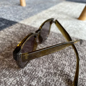 Bruna solglasögon från H&M - Snygga solglasögon från H&M med fyrkantig form och transparent brun plastbåge. Glasen är mörka och ger en cool vibe till din look. Perfekta för soliga dagar när du vill sticka ut lite extra.