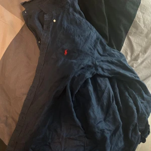 Marinblå linnéskjorta från Polo Ralph Lauren - Snygg marinblå linneskjorta från Polo Ralph Lauren i svalt linne. Skjortan har klassisk skjortkrage, knappar framtill och den ikoniska röda loggan broderad på bröstet. Perfekt för en chill och stilren look. Storleken är XL i barn så den passar även xs/s