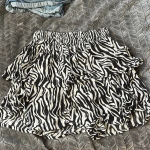 Zebramönstrad volangkjol från KappAhl - Superfin kort kjol från KappAhl med svartvitt zebramönster och flera volanger. Resår i midjan för skön passform. Perfekt för dig som vill sticka ut lite extra med en trendig look.