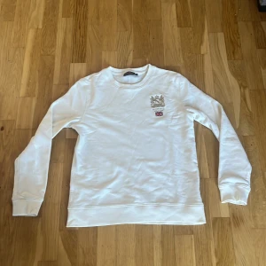 Vit sweatshirt från Morris, storlek S - Vit sweatshirt från Morris med broderad logga och brittisk flagga på bröstet. Klassisk rund halsringning och långa ärmar. Skön och stilren tröja i bomull, perfekt för en clean och avslappnad look.