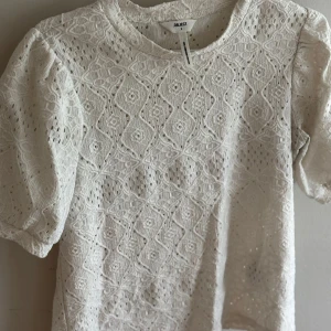 Vit spetsblus från Object - Superfin vit blus från Object med korta puffärmar och vackert spetsmönster över hela toppen. Blusen har rund halsringning och är tillverkad i ett luftigt material som känns både romantiskt och trendigt.