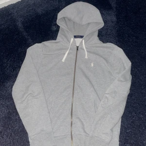 Grå hoodie från Ralph Lauren - Pris kan diskuteras Är öppen för byte, säljs eftersom den är för stor. Äkta och var en för stor födelsedags present. Storlek S men funkar för M med .Säljer en stilren grå hoodie från Ralph Lauren med dragkedja och vit logga på bröstet. Den har en justerbar huva med vita snören och långa ärmar. Perfekt för en avslappnad look.