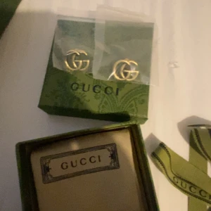 Gucci GG örhängen i guld - Säljer ett par ikoniska Gucci GG örhängen i guldtonad metall. Klassisk design med dubbla G-loggor, levereras i originalask, dustbag och presentpåse från Gucci. Perfekta för dig som vill ha en lyxig och tidlös accessoar med statement-känsla.