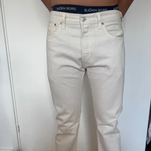 Levi's 501 vita jeans straight fit - Snygga vita Levi's 501 jeans med klassisk straight fit och hög midja. Jeansen har fem fickor, silverfärgade nitar och Levi's ikoniska läderpatch bak. Perfekta till sneakers eller boots för en clean och fräsch look.