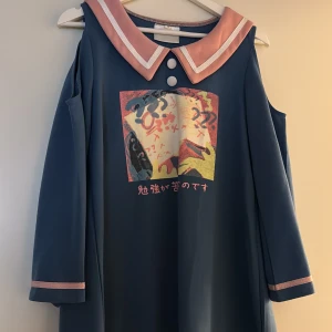 Blå sailor-klänning med tryck, M - Unik blå kortklänning/tunika med rosa sailor-krage och vita detaljer. Långärmad modell med cold shoulder och tryck framtill i pastellfärger samt japansk text. Snygga knappar vid halsen och rosa kantband på ärmar och nederkant. Perfekt för dig som gillar kawaii-stil! Den är storlek M men passar mer som en storlek S. Den passar perfekt som en tunika med en söt kol under!!<3