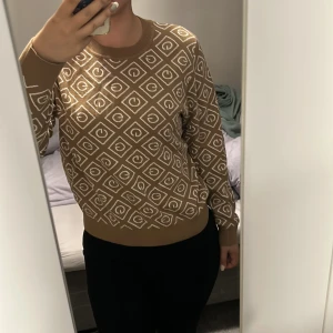 Beige stickad GANT tröja med mönster - Säljer en beige stickad tröja från GANT med vitt grafiskt mönster över hela tröjan. Rund halsringning, ribbade muddar och långärmad modell. Perfekt för dig som gillar en snygg och trendig look med lite retrovibbar🤎🤍