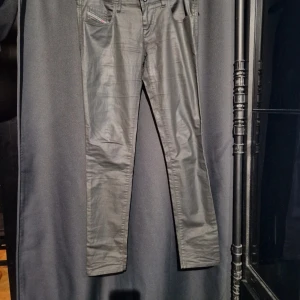 Svarta skinny jeans Diesel Grupee - Snygga svarta skinny jeans från Diesel, modell Grupee. Byxorna har låg midja, super slim passform och stretchigt material som sitter tajt. Klassisk femficksdesign och diskret glansig finish. Perfekta för dig som gillar en smal siluett och streetig vibe.