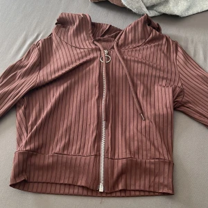 Brun ribbad hoodiejacka från SHEIN - Säljer en brun ribbad hoodiejacka från SHEIN i storlek XS. Jackan har dragkedja framtill, snörning i huvan och är tillverkad i mjuk polyesterblandning med lite stretch. Perfekt för en chill och avslappnad look.