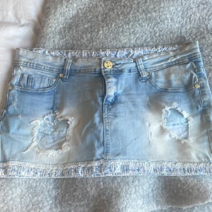Ljusblå jeanskjol med slitningar - Snygg ljusblå jeanskjol  med slitna detaljer och fransad nederkant. Klassisk fyrficksmodell med knapp och dragkedja framtill. Perfekt för dig som gillar en cool och avslappnad stil.