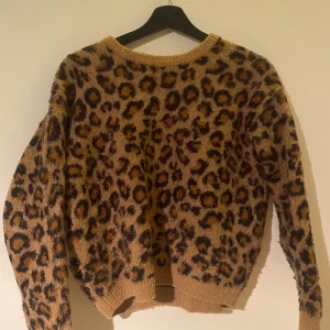 Leopardmönstrad stickad tröja H&M - Säljer en beige och brun stickad tröja från H&M med leopardmönster. Tröjan har rund hals, långa ärmar och ribbade muddar. Perfekt för dig som gillar djurmönster och vill ha en mysig och cool look.