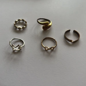 Fem trendiga ringar i silver och guld - Säljer ett set med fem snygga ringar i olika former och stilar. Två är i silverfärg, tre i guld. En har vågig design, en är öppen med twist, en har en fågel, en med oändlighetssymbol och en enkel öppen ring. Perfekta för att mixa och matcha till din stil.
