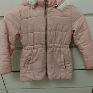 Ljusrosa pufferjacka för barn från H&M - Superfin ljusrosa pufferjacka för barn från H&M med mysig huva och fuskpälsdetalj. Jackan har dragkedja, två fickor och ett sött hjärta baktill. Perfekt för kalla dagar och riktigt gullig stil. Fodrad insida för extra värme.