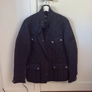 Svart quiltad jacka med fickor - Snygg svart quiltad jacka med fyra framfickor och silverfärgade knappar. Jackan har hög krage, dragkedja och tryckknappar framtill. Perfekt för höst och vinter, ger en clean och stilren look.