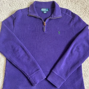 Lila half zip tröja Polo Ralph Lauren - Säljer en lila långärmad tröja från Polo Ralph Lauren i storlek S. Tröjan har en half zip-dragkedja och klassisk krage, med broderad grön logga på bröstet. Materialet är 100% bomull och passformen är normal. Perfekt för dig som gillar stilrena plagg.