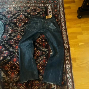 Levi's 507 mörkblå jeans bootcut - Säljer ett par Levi's 507 jeans i mörkblå tvätt med klassiska fem fickor och snygga slitningar. Jeansen har bootcut passform och är tillverkade i robust denim. Perfekta för dig som gillar en tidlös och avslappnad stil. 