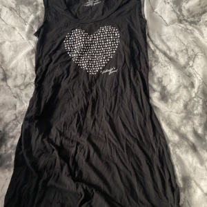 Svart pyjamas-klänning Victoria's Secret - Svart ärmlös klänning från Victoria's Secret med stort hjärtmotiv av vita stjärnor på bröstet. Mjuk och skön i bomull och polyester, perfekt för chill dagar. Rund halsringning och rak passform.