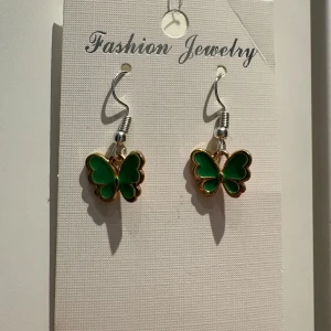 Gröna fjärilsörhängen med guldkant - Superfina örhängen med gröna fjärilar och guldfärgade kanter. Hängande modell med silvriga krokar, perfekt för dig som vill ha något unikt och färgglatt. Fjärilarna har en cool och lekfull vibe som lyfter din stil.