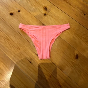 Rosa ribbad bikiniunderdel från C - Snygg bikiniunderdel i ljusrosa från C, storlek XS. Modellen har en klassisk, smal passform med ribbad struktur som ger en fräsch och trendig look. Perfekt för strandhäng och poolparty under sommaren. Materialet är mjukt och stretchigt syntet för bästa komfort.